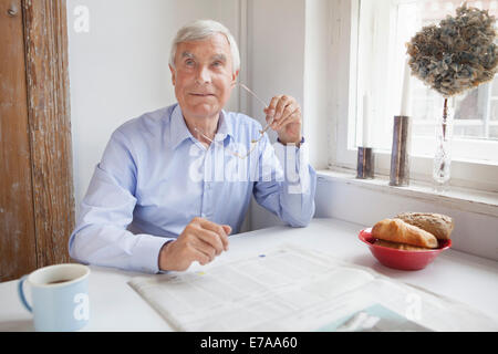Thoughtful senior man looking away while holding glasses at breakfast table Stock Photo