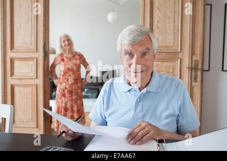 Portrait of surprised senior man checking financial documents at home with woman in background Stock Photo