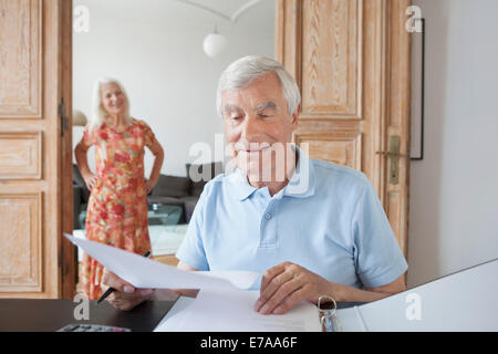 Senior man reviewing financial documents at home with woman in background Stock Photo