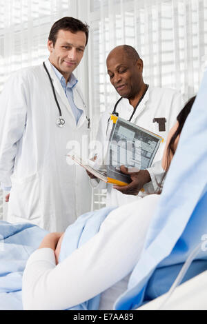 Two smiling doctors consulting over a patient lying in a hospital bed Stock Photo