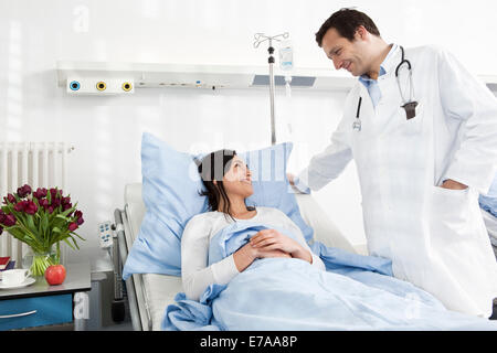 A doctor talking to a smiling patient lying in a hospital bed Stock Photo