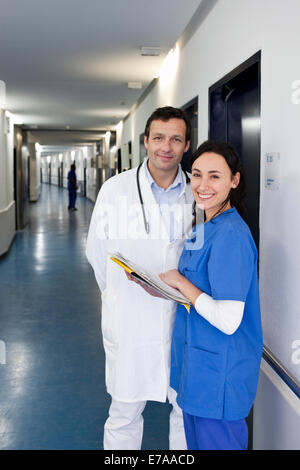 A nurse in scrubs consulting a doctor in a lab coat about a medical file, looking at camera Stock Photo