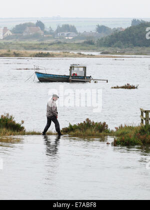 Thornham, Norfolk, UK. 11th Sept 2014. An exceptionally high tide floods the harbour, Staithe Road and the marshes at Thornham causing a little difficulty for a stranded walker. Credit:  Stuart Aylmer/Alamy Live News Stock Photo