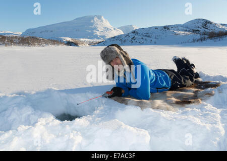 White man, 40-45 years old, icefishing, lying on a reindeer fur in Kiruna, Riksgränsen, Swedish lapland Stock Photo