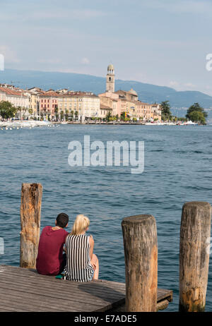 Young couple sit and enjoy the view and the afternoon sun on the lake shore of Lake Garda at Salo on the east side of the lake Stock Photo