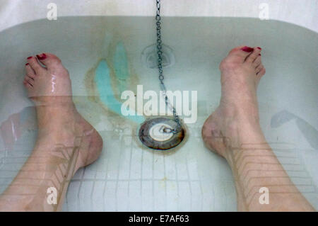 A view of a woman's feet with red nail varnish in the bath by the taps. Stock Photo