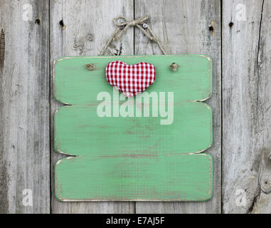 Red checkered heart on blank green sign hanging on old weathered wood door Stock Photo