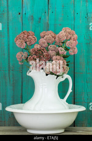 Antique white water pitcher and basin with flowers by weathered wooden green background Stock Photo