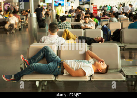 Chinese international Airport, China. Air passengers waiting resting sleeping napping in departure lounge chairs seats Stock Photo