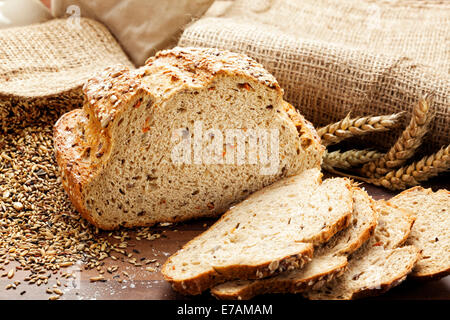 Whole grain organic bread and slices, burlap bags, wheat ears and grain in background Stock Photo