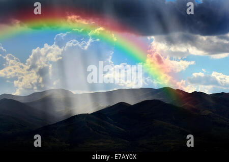 Sunlight rays from clouds falling on dark mountain range with Rainbow Stock Photo