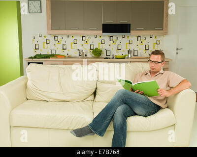 handsome Caucasian man reading book, lying on sofa Stock Photo