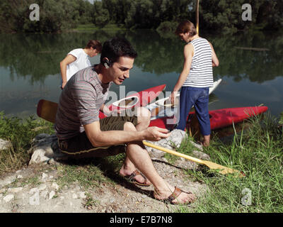 Young men with friends near river, discussing how to paddle in a kayak Stock Photo