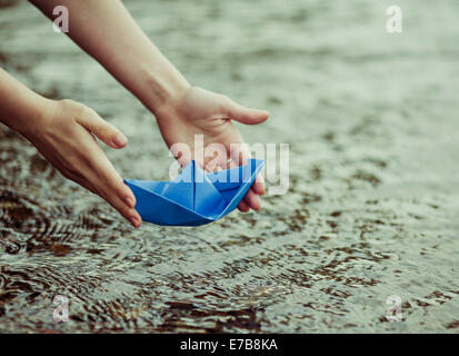 hands of a young woman with a paper boat by the lake in summertime (focus on the beat)