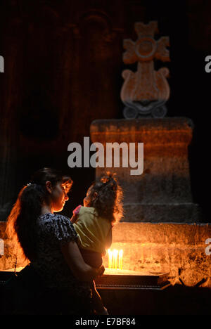 A mother holds her daughter in her harm in front of an altar with burning candles and a cross in a chapel at Geghard Monastery in Armenia on 29 June 2014. The monastery is of particular significance for the believers and followers of the Armenian Apostolic Church. The unabridged name of the monastery, Geghardavank, means 'the Monastery of the Spear' referring to the Holy Lance which had wounded Jesus at the Crucifixion. Apostle Thaddeus is supposed to have brought the spear to Armenia. There exists a UNESCO partnership with Lorsch Abbey in Hesse, Germany. Armeina was the first country to make  Stock Photo