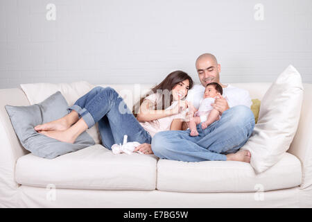 Young parents with little baby at home, sitting on cozy divan, enjoying family, loving couple with newborn daughter Stock Photo