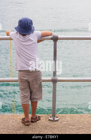 A young boy fishing for crabs on a pier with his back to the camera Stock Photo