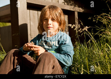 a boy with long brown hair sitting in garden Stock Photo