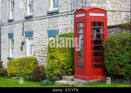 Traditional red British telephone box UK phone booth on the side of a road with houses in background; Nunnington North Yorkshire Stock Photo