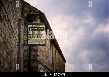 A weathered, British bus stop bus-stop sign on a pole post outside a house; shot against a cloudy autumnal sky. Stock Photo