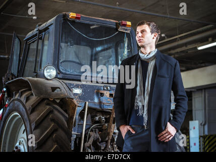 Fashion shot: a handsome young man wearing jeans and coat against the tractor Stock Photo