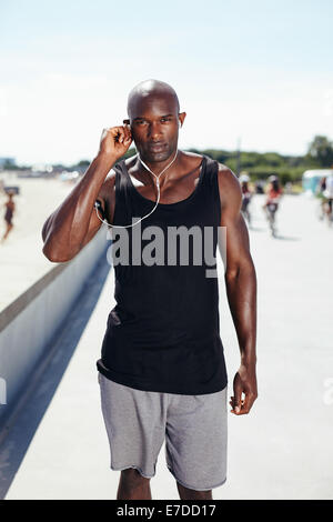 Image of fit young man at promenade wearing earphones to listen music. Fit young African man in sports wear. Stock Photo