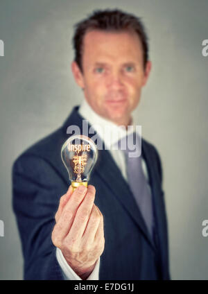 Businessman holding a lit lightbulb concept with the word Inspire. Stock Photo