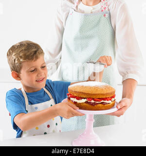 Boy sifting icing sugar over strawberry sponge cake Stock Photo