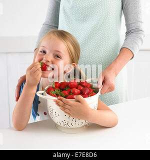 Young girl eating a strawberry from a bowl of strawberries Stock Photo