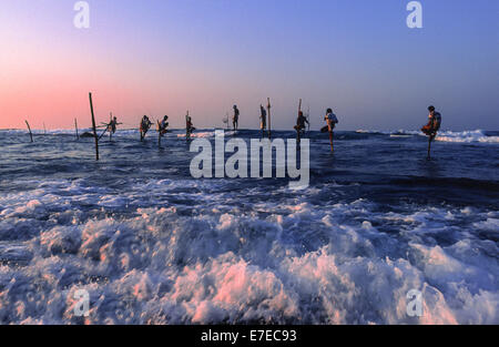 STILT FISHERMEN AT SUNRISE EARLY DAWN AND PINK TINGED WAVES IN SRI LANKA Stock Photo