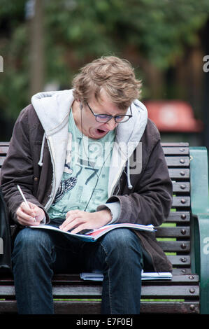 Yawning male student studying on a bench outside the state library in Melbourne, Australia, showing fatigue and exam stress during university study. Stock Photo