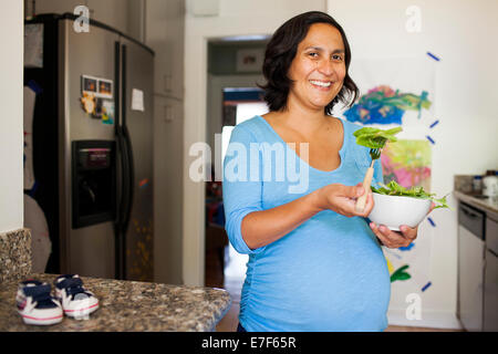Pregnant Hispanic woman eating salad in kitchen Stock Photo