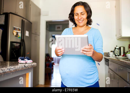 Pregnant Hispanic woman using tablet computer in kitchen Stock Photo