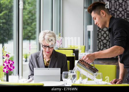 Waiter pouring water for customer in restaurant Stock Photo