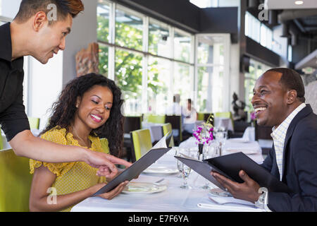 Waiter explaining menu to couple in restaurant Stock Photo
