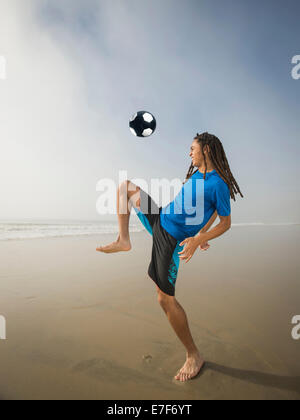 Black teenage boy playing with soccer ball on beach Stock Photo