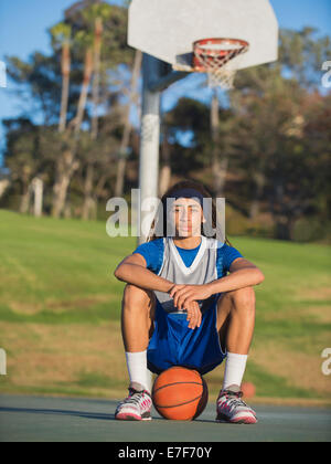 Black teenage boy sitting on basketball court Stock Photo