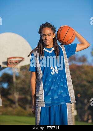Black teenage boy holding basketball on court Stock Photo