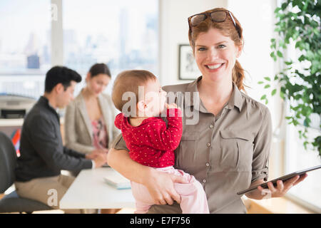 Businesswoman holding baby in office Stock Photo