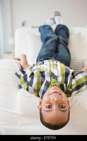 Mixed race boy laying upside-down on armchair Stock Photo