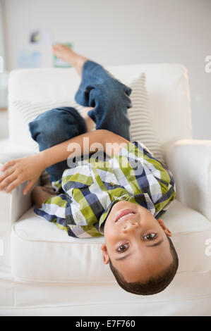 Mixed race boy laying upside-down on armchair Stock Photo