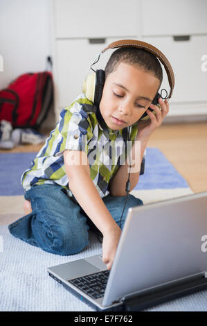 Mixed race boy listening to headphones on laptop Stock Photo