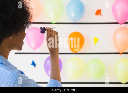African American woman popping balloons with dart Stock Photo