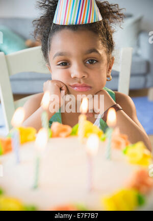 African American girl pouting at birthday cake Stock Photo