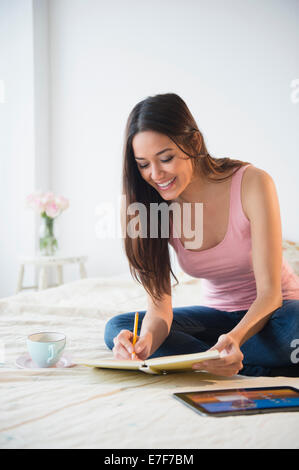 Woman taking notes with tablet computer on bed Stock Photo
