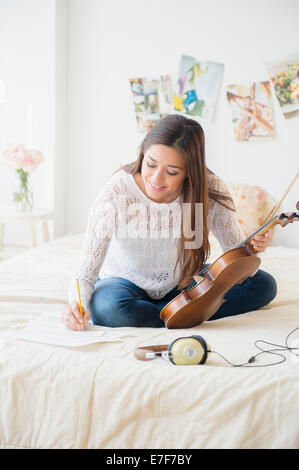 Woman playing violin and taking notes on bed Stock Photo