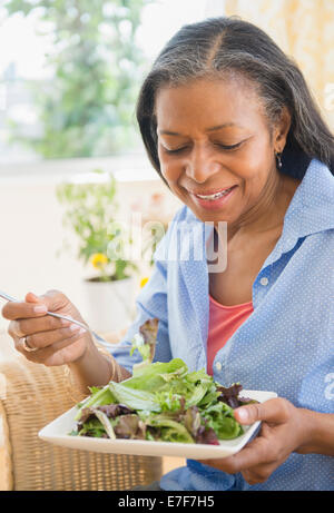 Mixed race woman eating salad on sofa Stock Photo