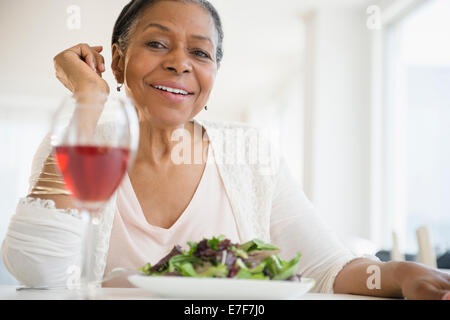 Mixed race woman eating salad at table Stock Photo