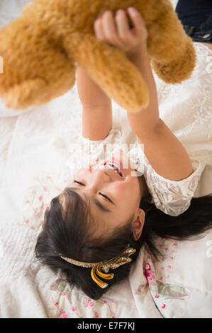 Filipino girl playing with teddy bear on bed Stock Photo