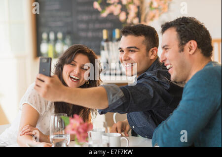 Hispanic friends taking pictures with cell phone in cafe Stock Photo
